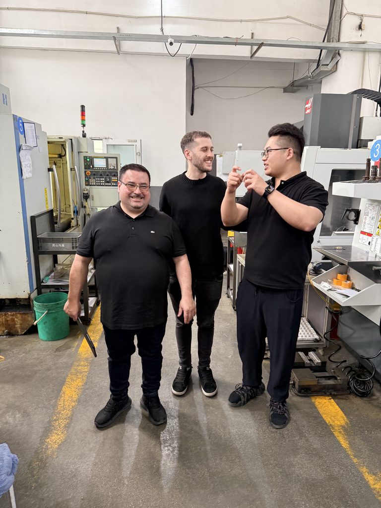 Jinxi staff discussing a machined part with visitors beside CNC equipment.